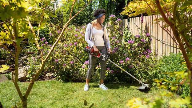 Kvinna i trädgårdsmiljö som använder Hondas batteridrivna grästrimmer.