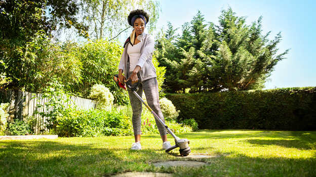 Kvinna som använder Hondas batteridrivna grästrimmer i trädgårdsmiljö.