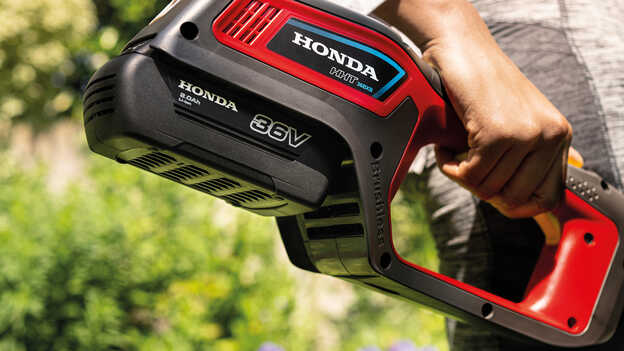 Närbild av en modell som håller Hondas batteridrivna grästrimmer