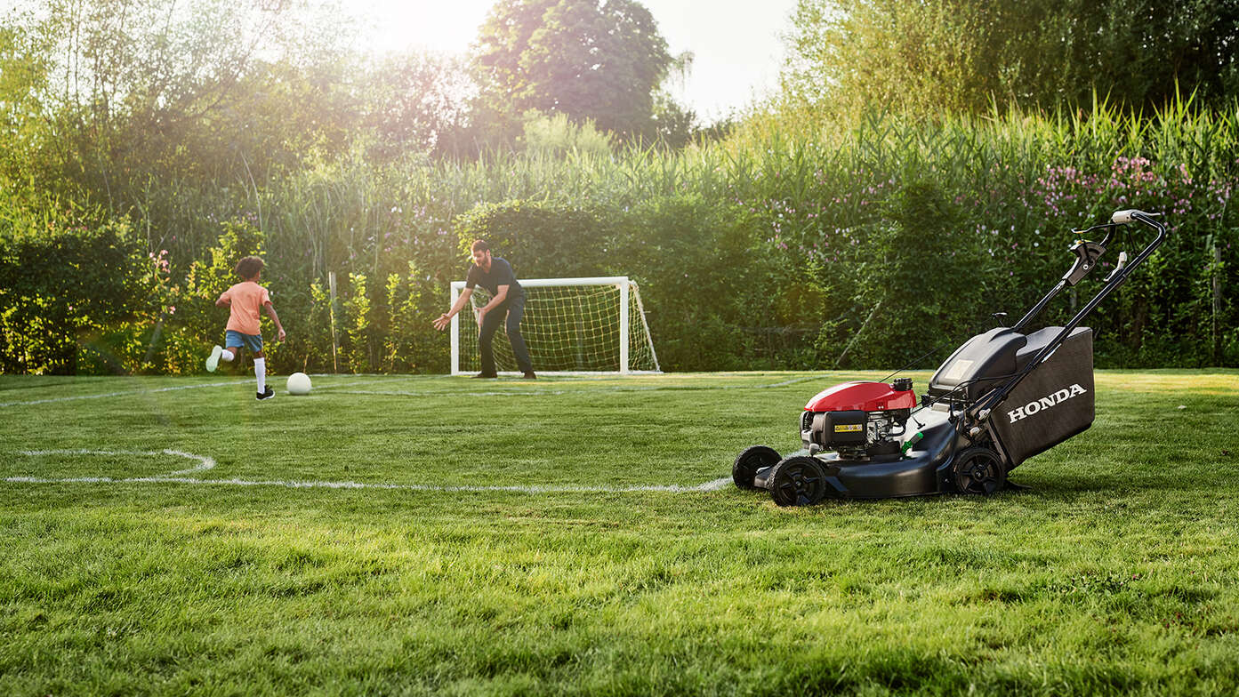 Man och barn spelar fotboll vid en Honda HRN i trädgården. 