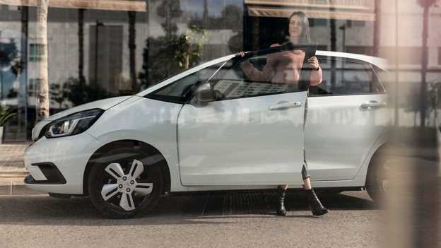 Vy från sidan av Honda Jazz parkerad med en kvinna som öppnar dörren