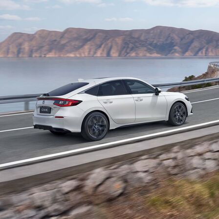 Sidovy av Honda Civic e:HEV som kör längs en kustväg.