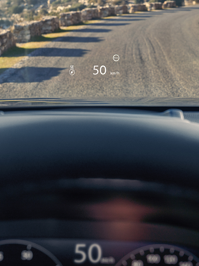 En vy från förarplatsen som visar en head-up-display (HUD) som projicerar "50 km/h" och en kompass på vindrutan ovanför en grusväg.
