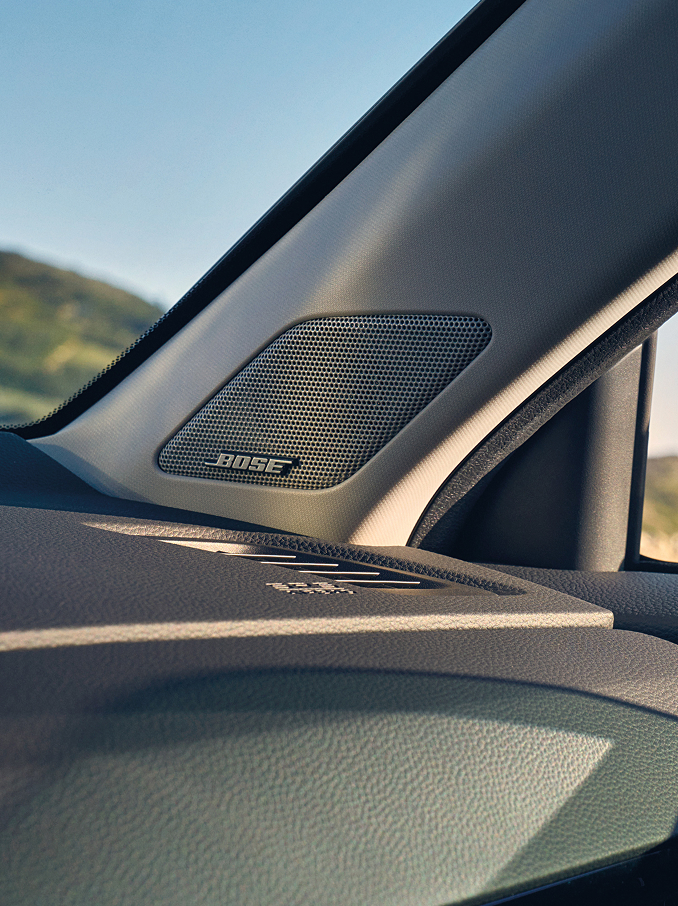  En närbild av en Bose-högtalare integrerad i A-stolpen på en bil, placerad nära instrumentpanelen och vindrutan.