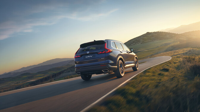 Sidovy bakifrån av en blå CR-V Hybrid SUV i bergsmiljö.