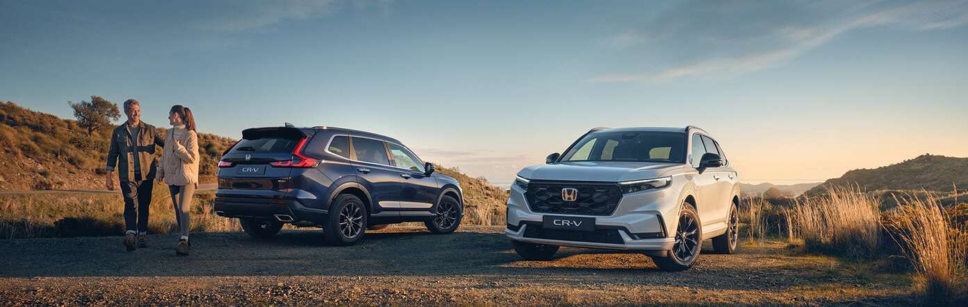 En blå och en vit Honda CR-V plug-in hybrid som står parkerade ute i naturen. En man och en kvinna är på väg ut på äventyr.