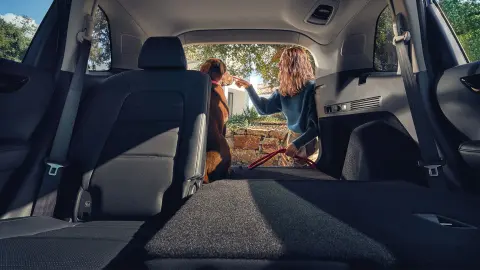 CR-V Hybrid SUV med baksätet fällt, kvinna och hund vid det öppna bagageutrymmet. 