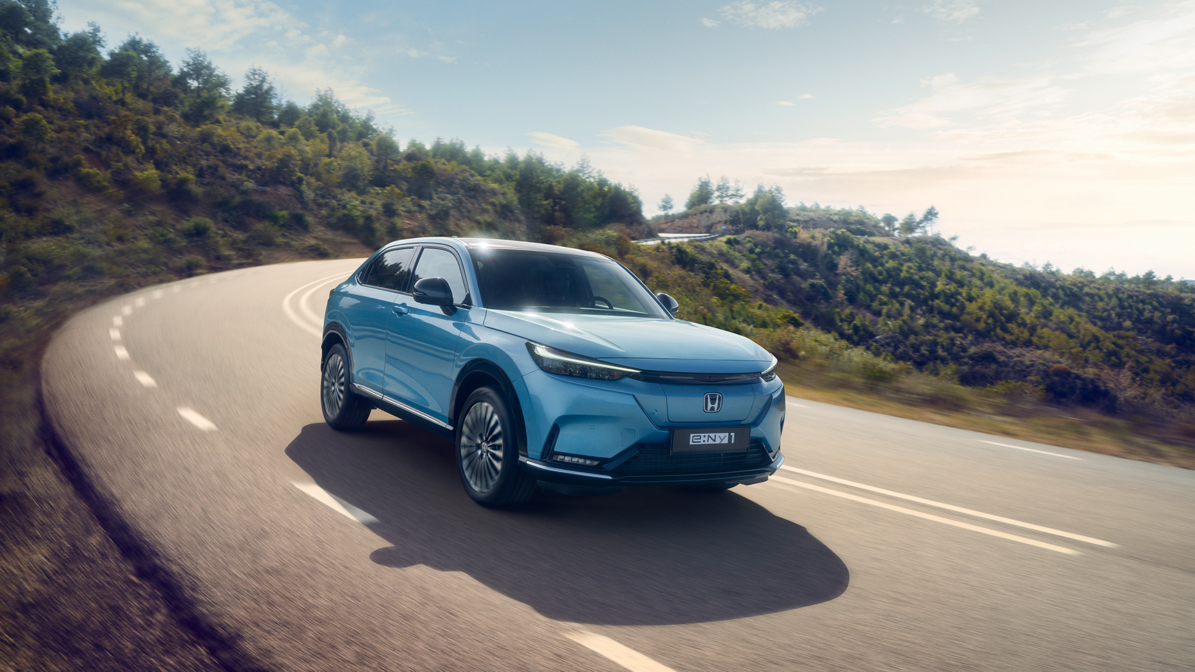 Vy framifrån av Honda e:Ny1 som kör längs vägen i landsbygdsmiljö.