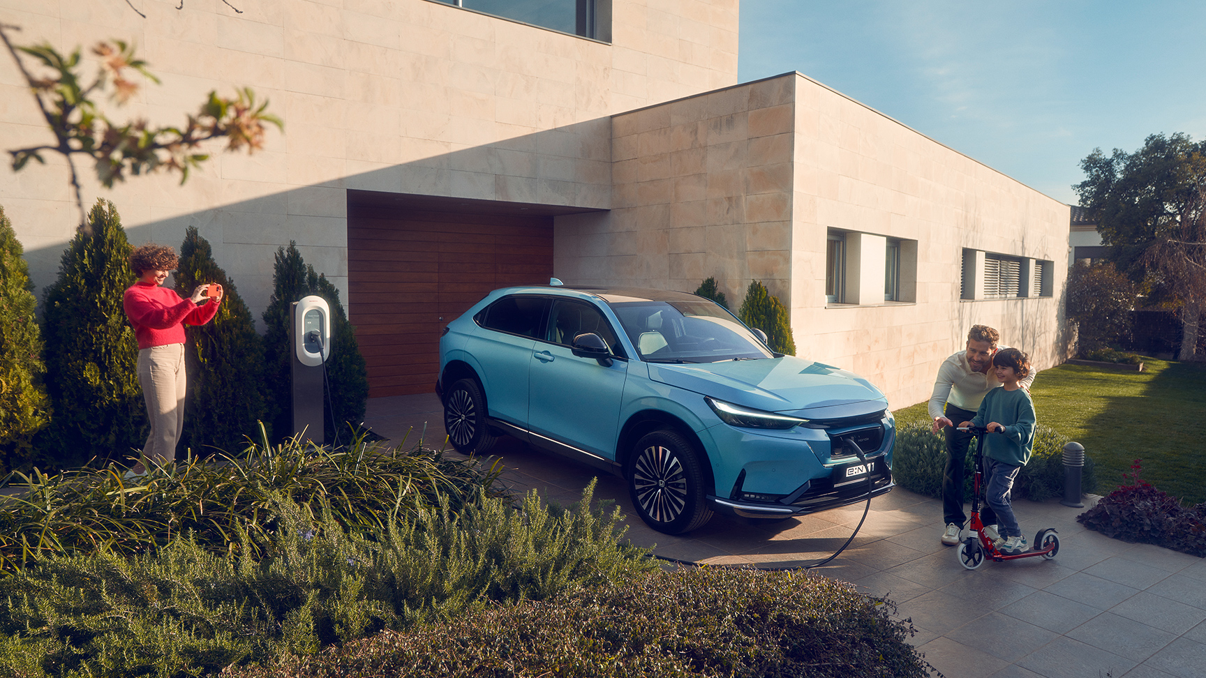 Familj som leker på uppfarten bredvid Honda e:Ny1 som laddar på uppfarten.