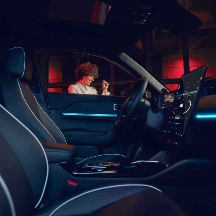Upplyst inredning i Honda e:Ny1 på natten med modell utanför fönstret.