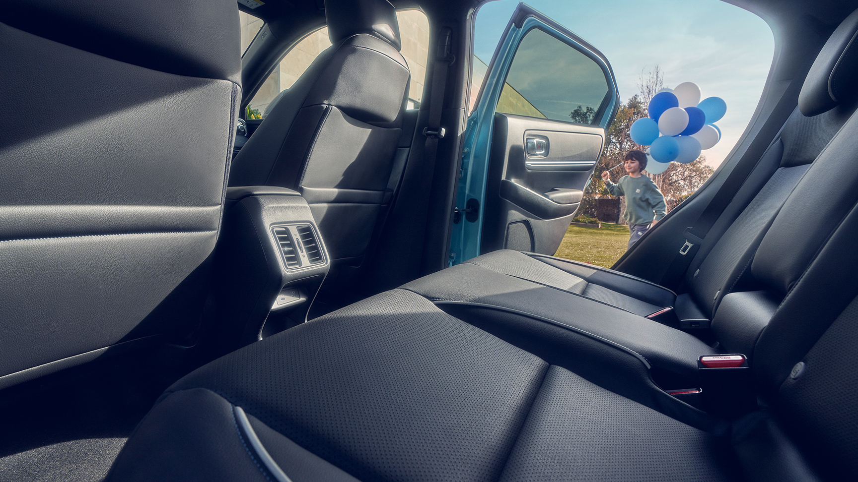 Närbild av baksätet i Honda e:Ny1, med barn som går förbi öppen dörr med ballonger.