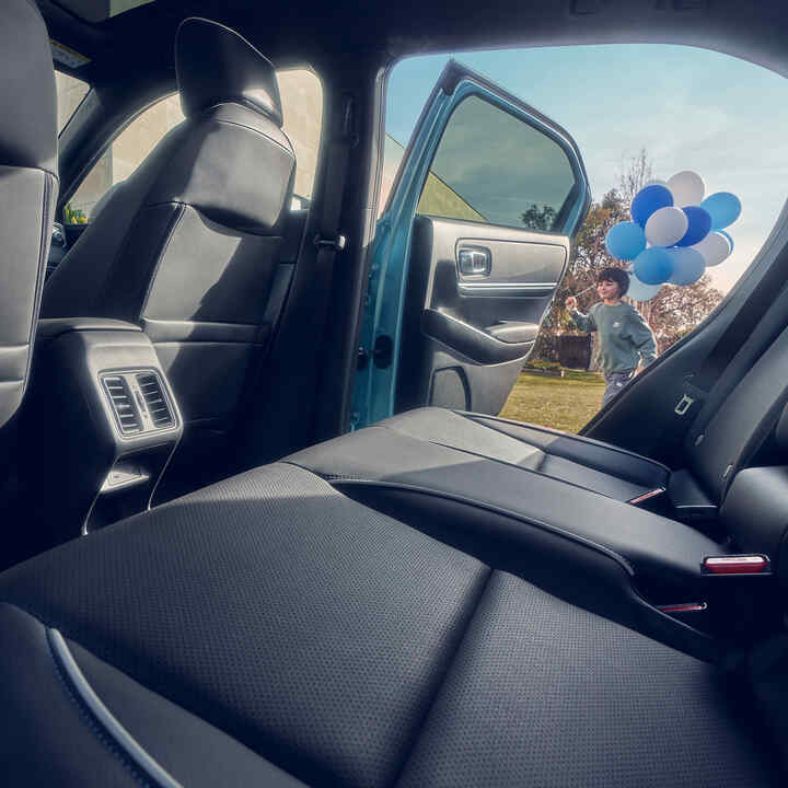 Närbild av baksätet i Honda e:Ny1, med barn som går förbi öppen dörr med ballonger.