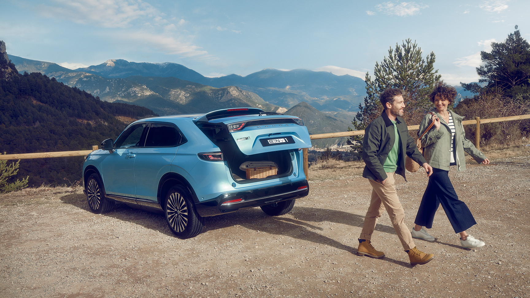 Vy snett bakifrån av Honda e:Ny1 i bergig miljö med ett par som går iväg.