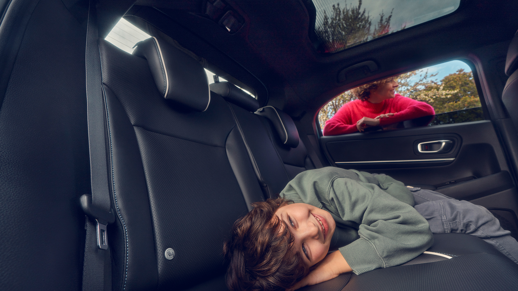 Barn som ligger på baksätet med mamma som står i fönstret på Honda e:Ny1.