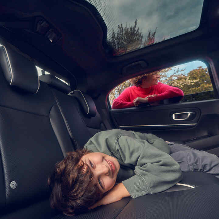 Barn som ligger på baksätet med mamma som står i fönstret på Honda e:Ny1.