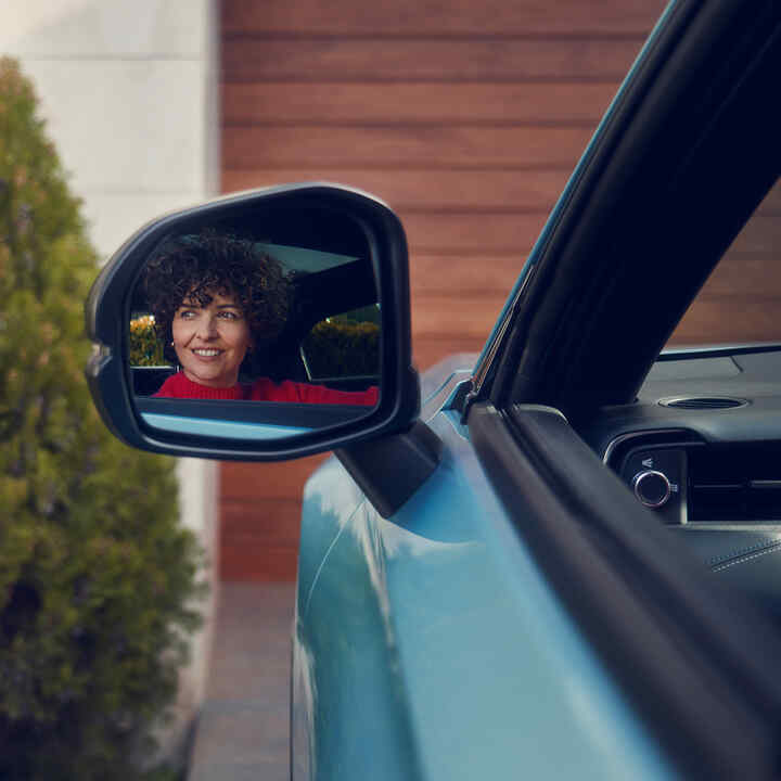 Kvinnors reflektion i dörrbackspegeln på Honda e:Ny1.