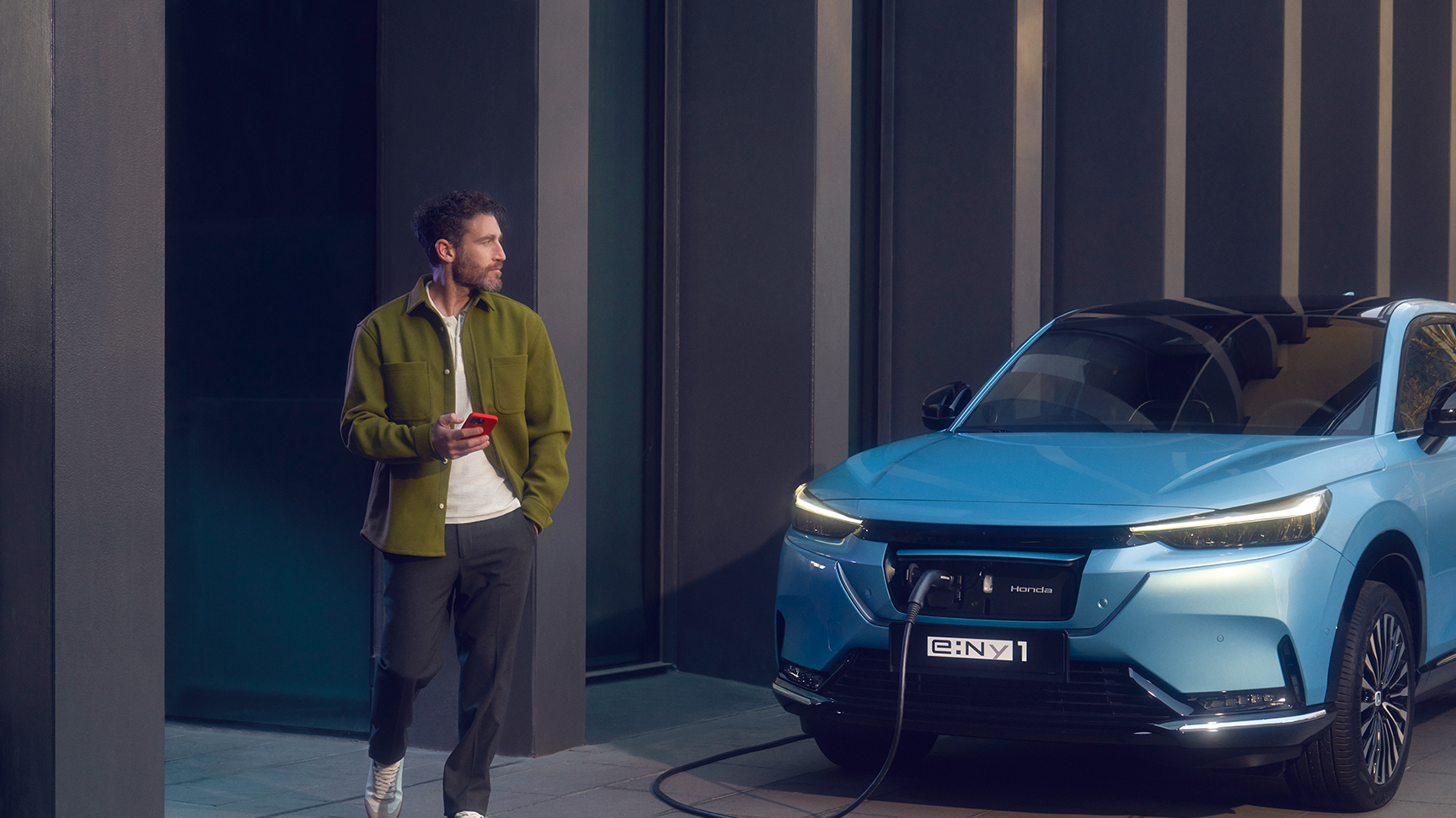 Man som går förbi en laddande Honda e:Ny1 framför en byggnad.