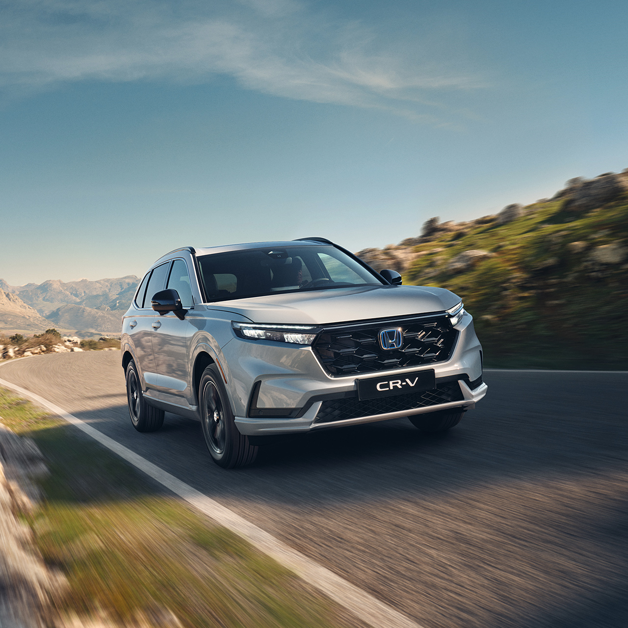 Vit CR-V-pluginhybridbil som kör på vägen i bergsmiljö.
