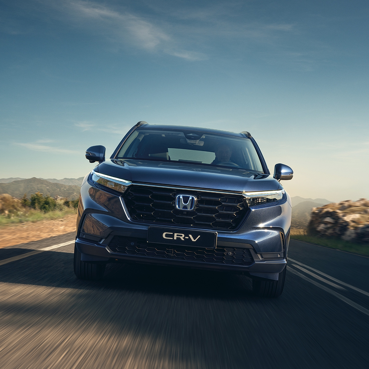 Vy framifrån av CR-V-hybrid som kör på vägen i bergsmiljö.