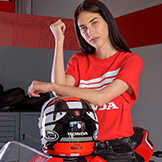 Kvinna som bär en röd Honda-tröja och lutar sig mot en Honda-motorcykelhjälm.
