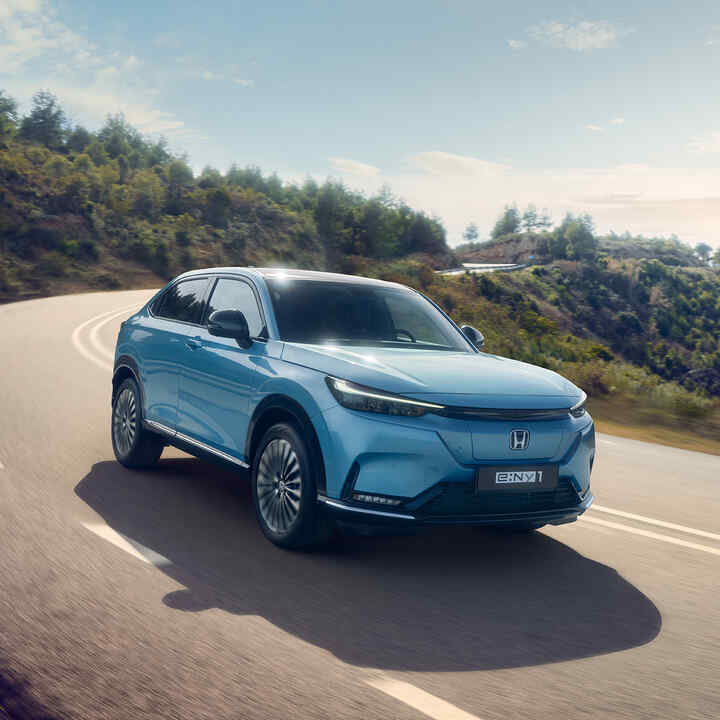Trekvarts vy framifrån av en Honda e:Ny1 som kör i ett bergigt område.