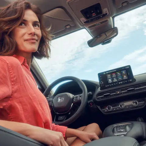 Kvinna i förarsätet som använder infotainmentskärmen i Honda ZR-V Hybrid.