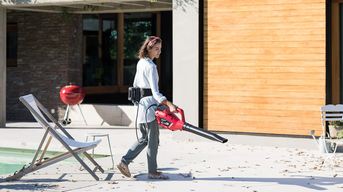 Person som bär Hondas batteridrivna bälte och använder en lövblåsare i trädgårdsmiljö.