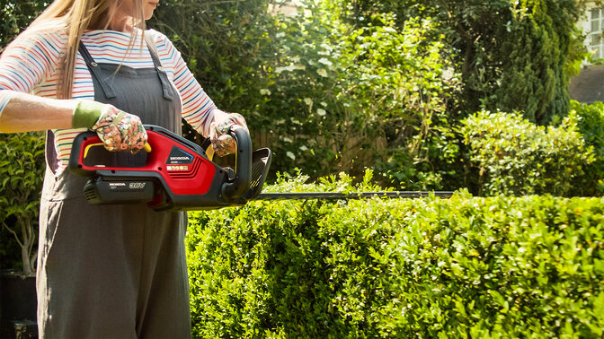 Kvinna som klipper en häck med Hondas batteridrivna häcksax i trädgårdsmiljö