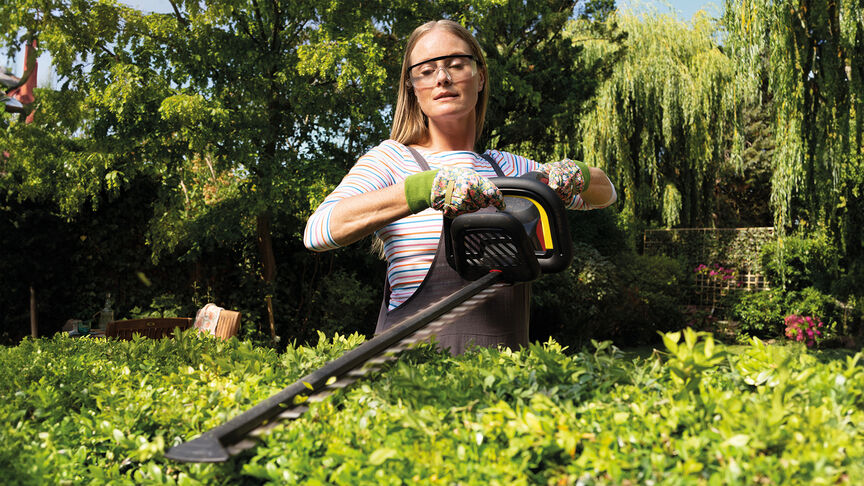 Kvinna som använder en batteridriven Honda-häcksax för att klippa en häck i trädgården.