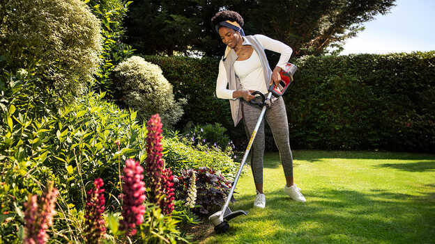Kvinna som använder Hondas batteridrivna grästrimmer med växtskyddet på gräs i en trädgård.