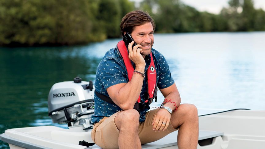 Man i liten båt laddar sin telefon via utombordsmotorn från Honda samtidigt som han talar