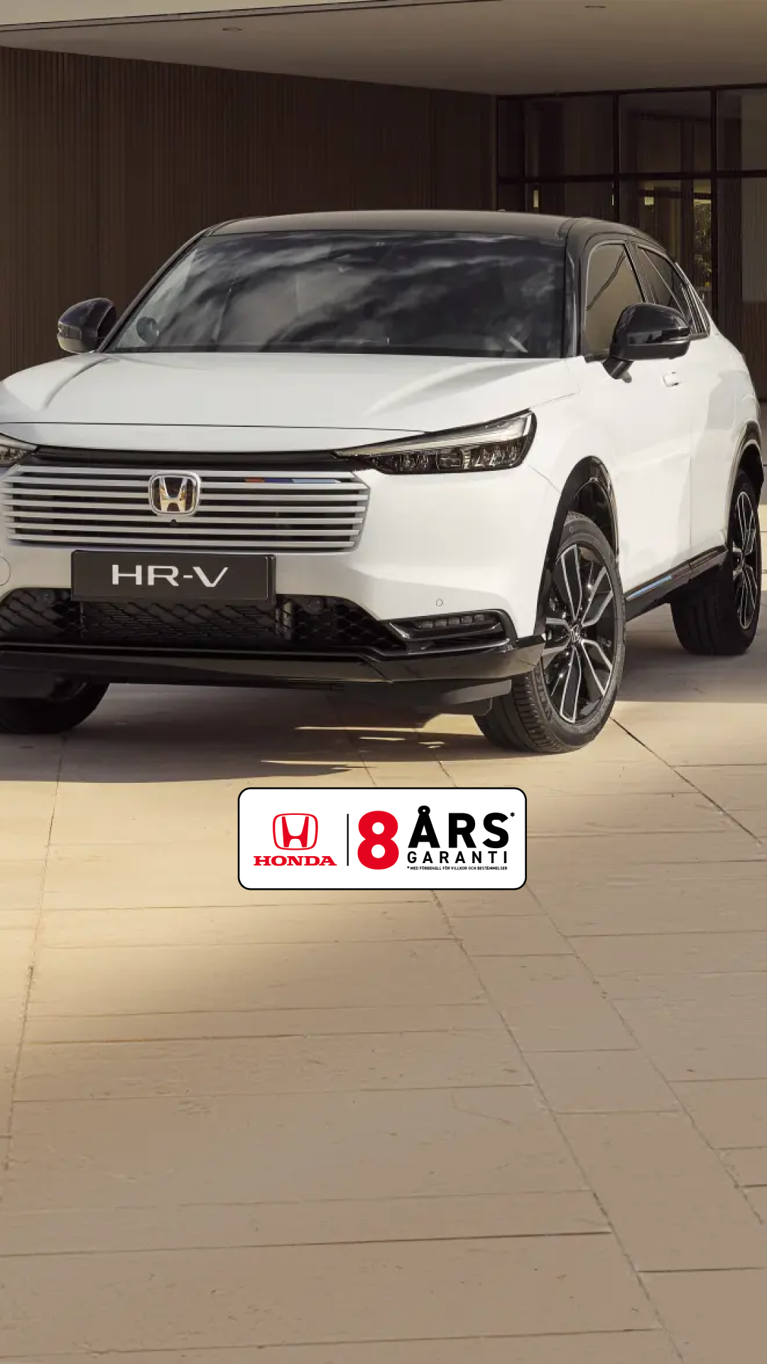 En vit Honda HR-V SUV parkerad framför en modern byggnad med beigekaklade väggar. Bilen står i vinkel för att visa upp sin eleganta design och karakteristiska grill.